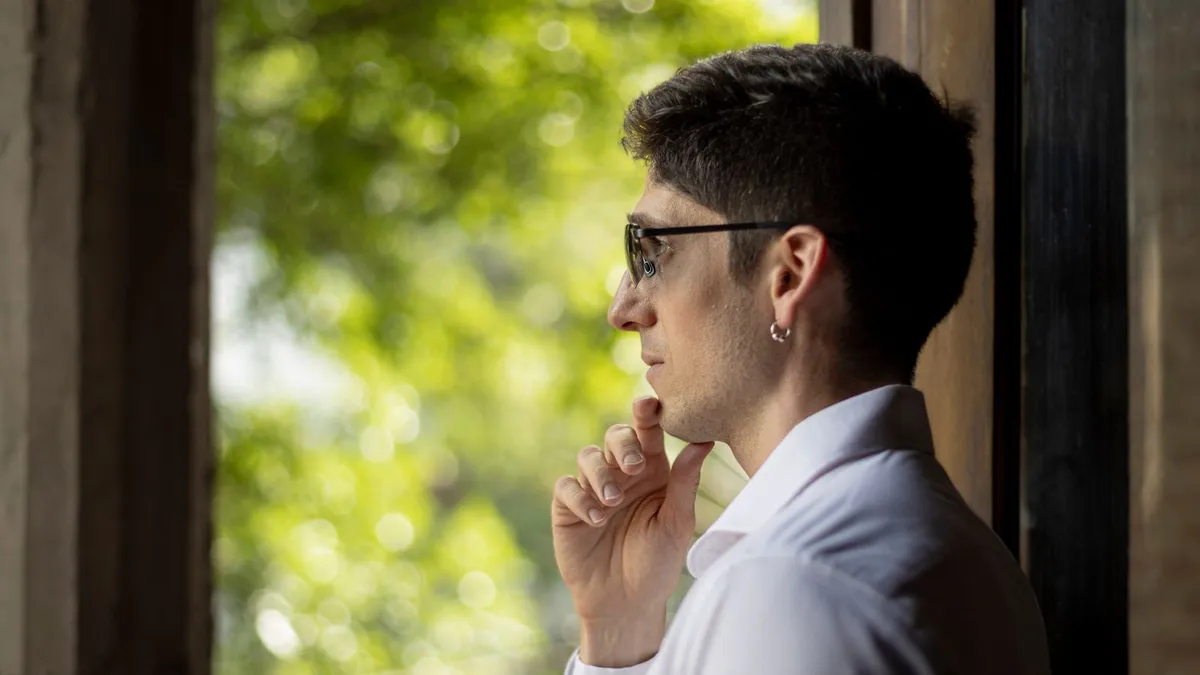 Man thinking by a window at home while weighing the debt help unemployed Canadians can get after a job loss