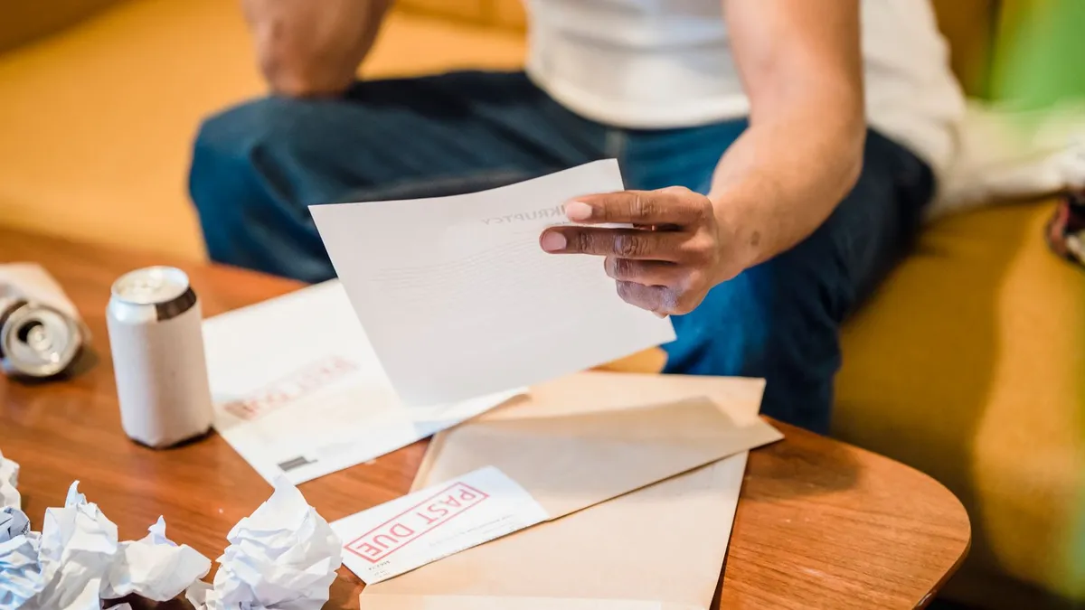 Worried man reading collection letters at his kitchen table after choosing to stop paying credit cards